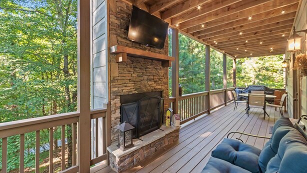 A covered deck with a stone fireplace, outdoor seating, and a TV mounted on the wall. - Cozy 5BR Cabin with 3 Fireplaces, Hot Tub, Fenced Yard (Ellijay)