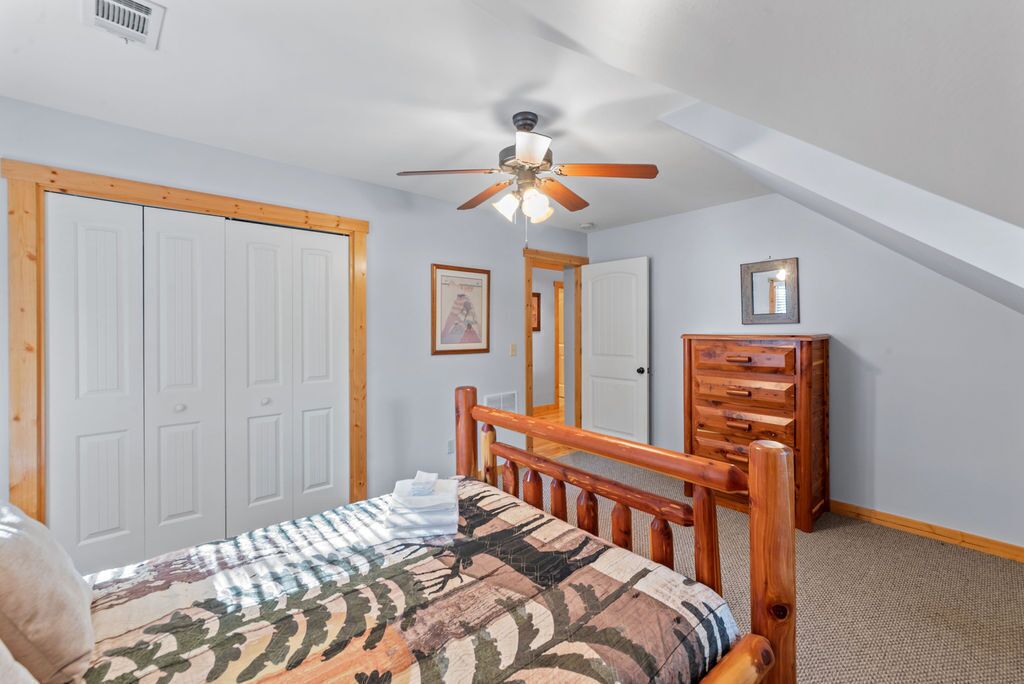 A bedroom with a bed, wooden headboard, ceiling fan, white wardrobe, and a dresser.