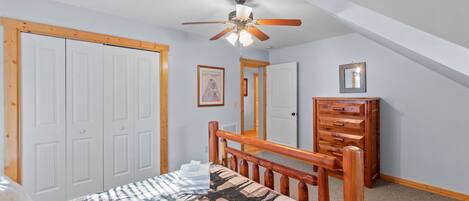 A bedroom with a bed, wooden headboard, ceiling fan, white wardrobe, and a dresser.