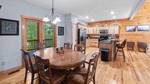 A spacious kitchen with wooden cabinets, a central island, and a dining area with a round table and chairs. - Cozy 5BR Cabin with 3 Fireplaces, Hot Tub, Fenced Yard (Ellijay)