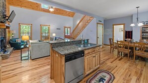 A spacious living area with a kitchen island, wooden flooring, and a staircase leading to another level. - Cozy 5BR Cabin with 3 Fireplaces, Hot Tub, Fenced Yard (Ellijay)