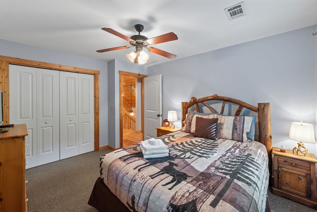 A bedroom with a bed, wooden headboard, ceiling fan, bedside lamps, and a wooden nightstand.