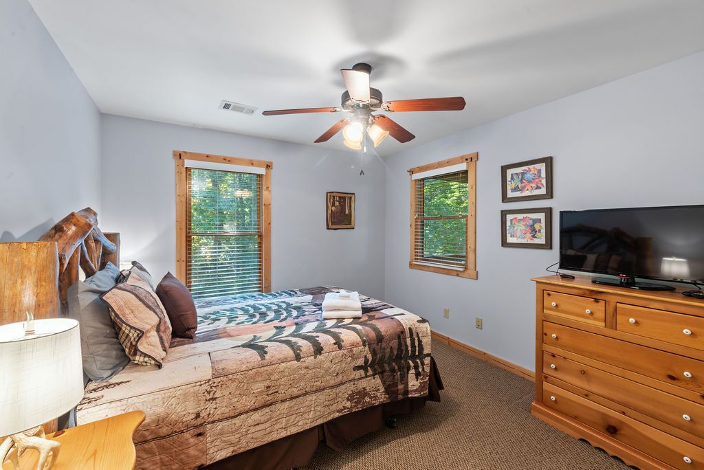 A bedroom with a bed, a ceiling fan, a dresser, and two windows.