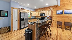 A modern kitchen with wooden cabinets, a stainless steel refrigerator, a microwave, and a granite countertop. - Cozy 5BR Cabin with 3 Fireplaces, Hot Tub, Fenced Yard (Ellijay)