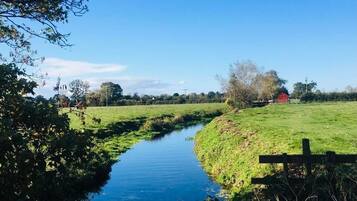 Een landelijk landschap met een smal waterkanaal, groene velden en een rode bebouwing in de verte.