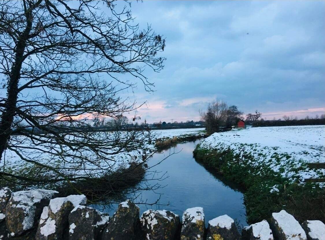 Une rivière dont les berges sont couvertes de neige, avec un mur de pierre au premier plan.