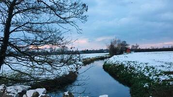 Une rivière dont les berges sont couvertes de neige, avec un mur de pierre au premier plan.