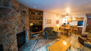 A cozy living room with a stone fireplace, a wooden coffee table, a comfortable sofa, and a dining area with a table and chairs. - 1BR Cascade Village condo with pool, hot tub, fireplace, and full kitchen. (Durango)