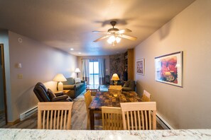 A dining area with a wooden table and chairs, a ceiling fan, and a stone fireplace. - 1BR Cascade Village condo with pool, hot tub, fireplace, and full kitchen. (Durango)