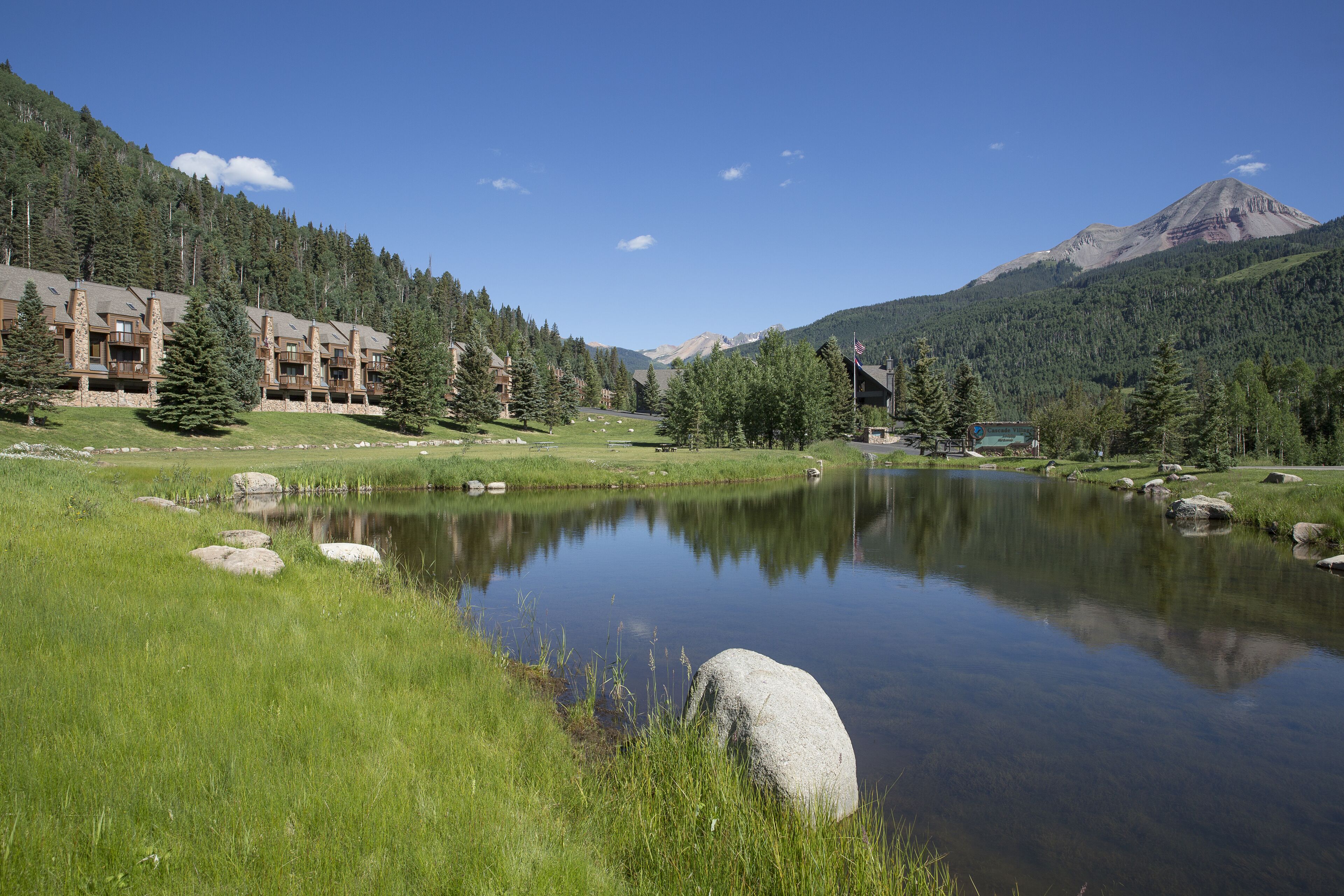 A lakeside view with a lodge, a mountain in the background, and a clear sky.