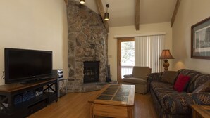 A living room with a stone fireplace, a television, a sofa, and a lamp. - Cascade Village 318 - Pool and Hot Tub Access (Durango)