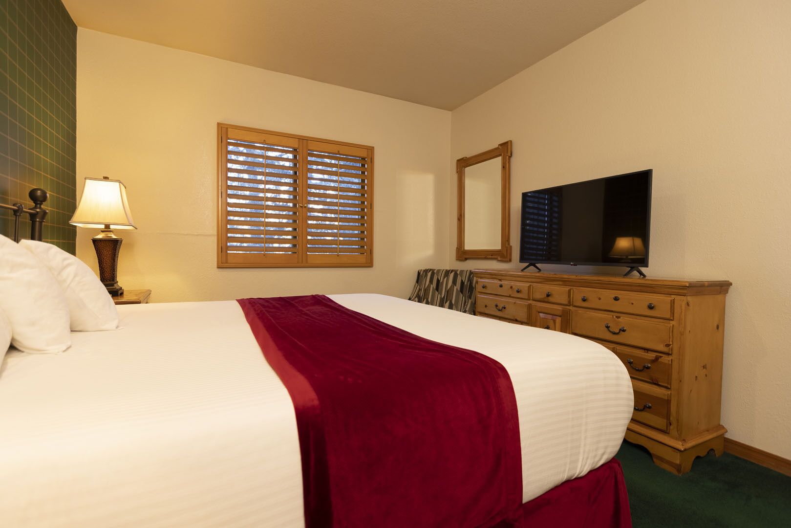 A hotel room with a bed, a dresser, a television, and a window with blinds.
