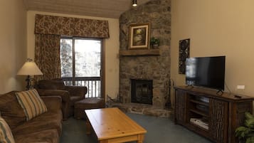 Un salon chaleureux avec une cheminée en pierre, un téléviseur et un canapé confortable.