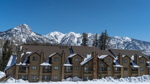 A row of wooden multi-story buildings with balconies, set against a backdrop of snow-covered mountains. - Cascade Village 357: One Bedroom mountain-view condo with pool, hot tub & balcony. (Durango)