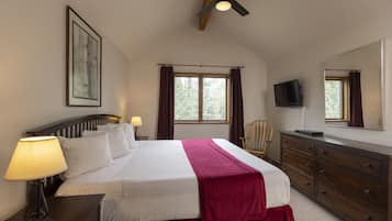 Une chambre à coucher comprenant un lit, des lampes de chevet, une commode, un téléviseur et une fenêtre avec des rideaux.