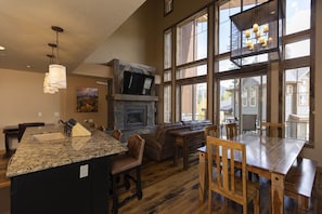 A spacious kitchen with granite countertops, a built-in island with a sink, and a stone fireplace. There is a large dining area with wooden tables and chairs, and a cozy seating area with a leather couch. - Alpenglow 18 - Managed by Purgatory (Durango)