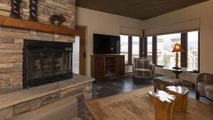 A living room with a stone fireplace, a flat-screen TV, and a large window with a view.