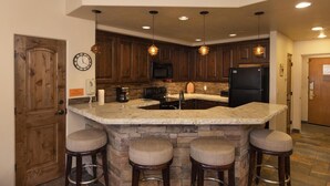 A kitchen with dark wood cabinets, a granite countertop, a black refrigerator, and a built-in island with stools.