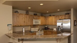 A kitchen with wooden cabinets, a granite countertop, a stainless steel refrigerator, and a built-in oven. - Eolus 525 - Managed by Purgatory Result (Durango)