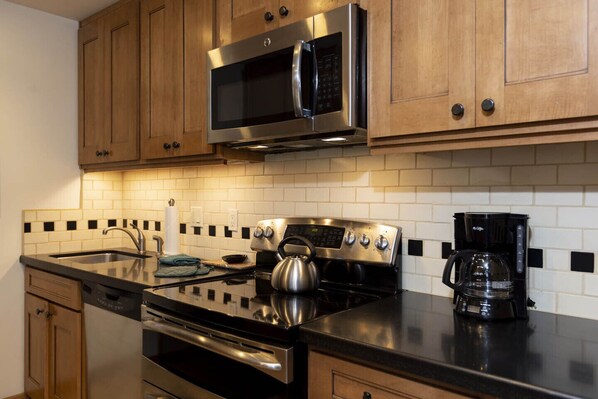 A modern kitchen with wooden cabinets, a stainless steel microwave, a kettle, a coffee maker, and a dishwasher. - Purgatory Resort Retreat with pool, hot tub, and balcony - Three Bedroom (Durango)