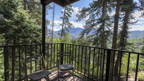 A wooden deck with two tables and a bench, surrounded by a metal railing, overlooking a forested mountain landscape. - Purgatory Resort Retreat with pool, hot tub, and balcony - Three Bedroom (Durango)