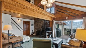Una sala de estar acogedora con chimenea, una escalera y vistas a las montañas.