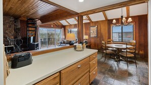 Una cocina con una isla de madera, un comedor con una lámpara de araña y vistas a través de las ventanas.
