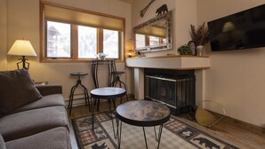 Una sala de estar acogedora con chimenea, televisor montado en la pared y un amplio ventanal con vistas a un paisaje nevado.