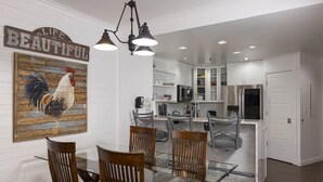 A dining area with a glass table and wooden chairs, a kitchen with white cabinets, and a wall-mounted rooster painting. - Kendall 239 - Managed by Purgatory Resort (Durango)