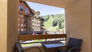 A balcony with a view of a multi-story building, a ski slope, and a chair with a table. - Kendall 239 - Managed by Purgatory Resort (Durango)