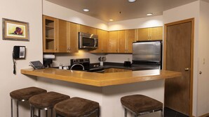 A compact kitchen with wooden cabinets, a stainless steel refrigerator, a microwave, and a stove. There are three stools at the counter. - Cozy One Bedroom Ski Condo with Amazing Mountain Views (Durango)