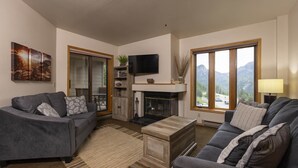 A living room with two sofas, a fireplace, a flat-screen TV, and large windows offering a mountain view. - Cozy One Bedroom Ski Condo with Amazing Mountain Views (Durango)