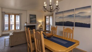 Ein Essbereich mit Holztisch, Stühlen und einer Kandelaber. Es gibt Fenster mit Vorhängen, einen Kamin und Kunstwerke an der Wand.