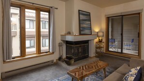 Ein Wohnzimmer mit Kamin, einer Couch, einem Couchtisch und großen Fenstern.