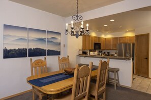 A dining area with a wooden table, chairs, and a chandelier. There are three paintings on the wall, a kitchen with wooden cabinets, and a refrigerator. - Kendall 541 - Managed by Purgatory Resort (Durango)