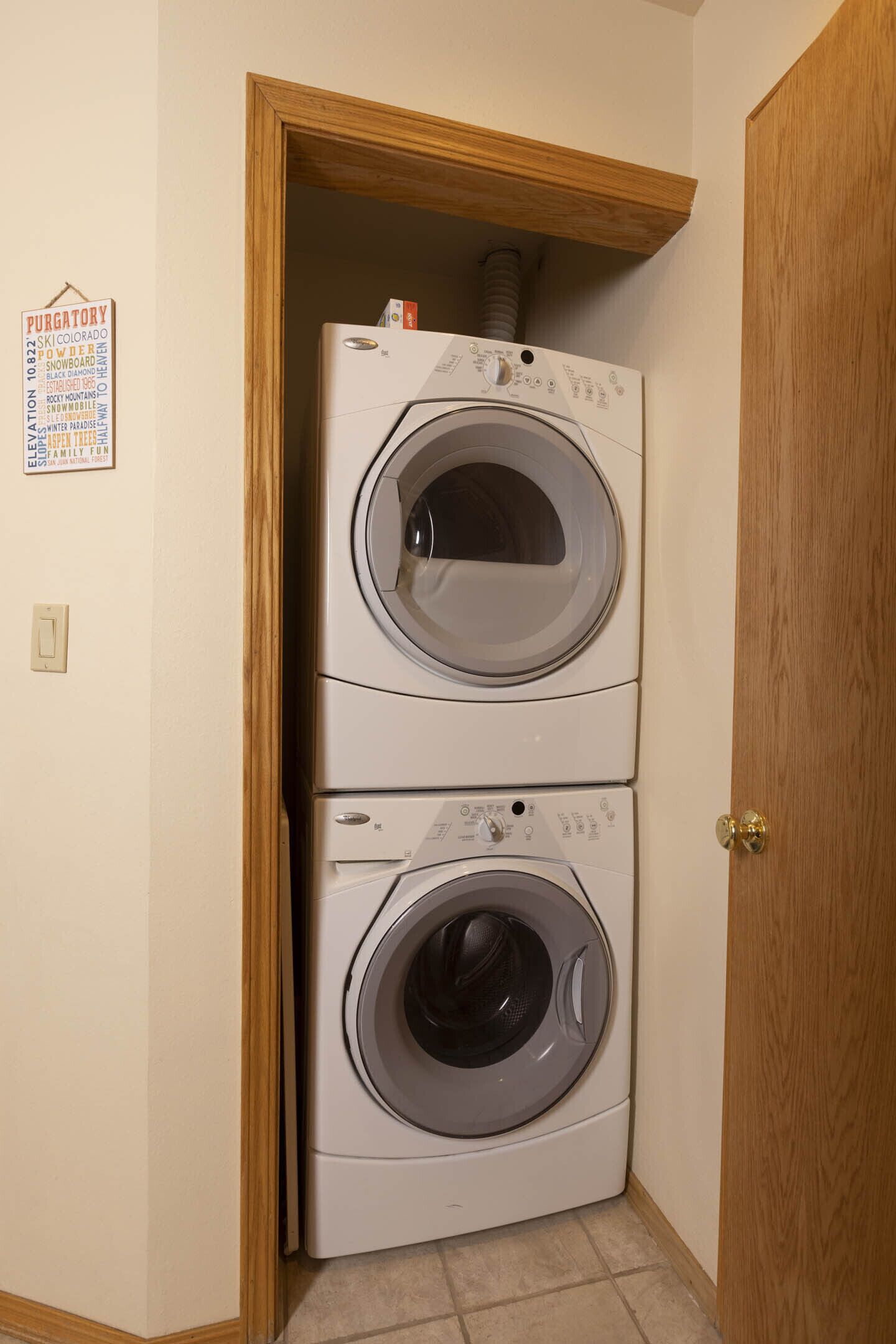 A laundry room with two stacked front-loading washing machines and a wooden door.