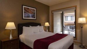 Ein Hotelzimmer mit einem großen Bett, zwei Nachttischlampen, einem gerahmten Bild an der Wand und Blick auf einen Außenbereich durch eine Schiebetür.