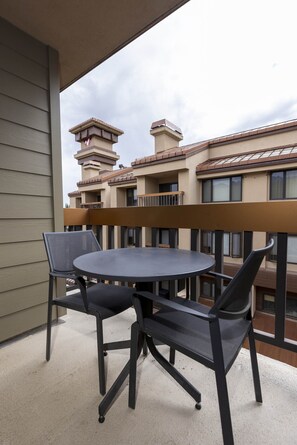 Ein Balkon mit rundem Tisch und vier Stühlen, mit Blick auf ein Gebäude mit mehreren Balkonen und einem turmartigen Aufsatz.