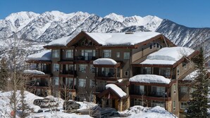 Un hotel de varios pisos con tejado nevado y múltiples balcones, rodeado de montañas.