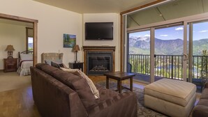Una sala de estar con chimenea, sofá, televisión y balcón con vista a la montaña.