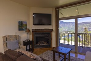 Una sala de estar con chimenea, televisor y balcón con vista a la montaña.