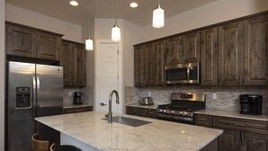 A modern kitchen with dark wooden cabinets, stainless steel appliances, a granite countertop, and pendant lighting. - Tacoma Vista 147 - Managed by Purgatory Result (Durango)