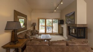 Una sala de estar con sofá, mesa de centro, chimenea, televisor y puerta corrediza de vidrio que da a un patio exterior.