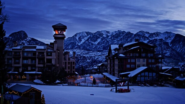 A snow-covered mountain resort with multiple buildings, including a prominent tower with a lit lantern. - Village Center 402 - Managed by Purgatory Resort (Durango)