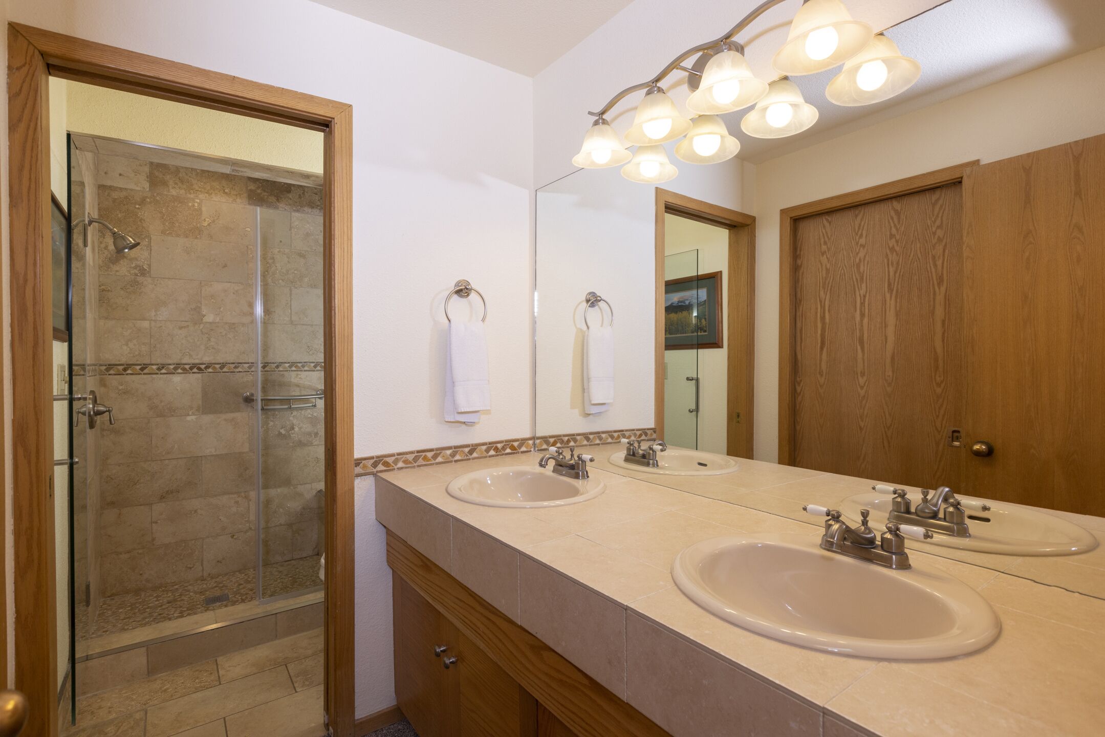 A bathroom with two sinks, a glass shower enclosure, and a wooden door.