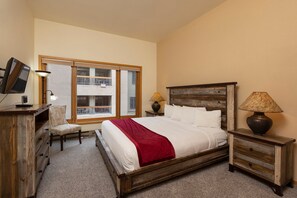 A bedroom with a bed, a desk, a chair, a TV, and a window.