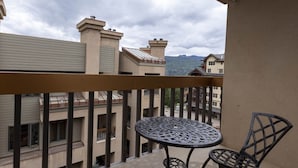 Un balcon avec une table ronde et deux chaises, donnant sur un quartier résidentiel composé de plusieurs immeubles et avec une montagne en arrière-plan.
