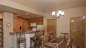 Un coin repas avec une table et des chaises en bois, une cuisine équipée d’un four à micro-ondes et d’une cuisinière, et une horloge au mur.