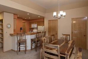 Un coin repas avec une table et des chaises en bois, une cuisine équipée d’un four à micro-ondes et d’une cuisinière, et une horloge au mur.