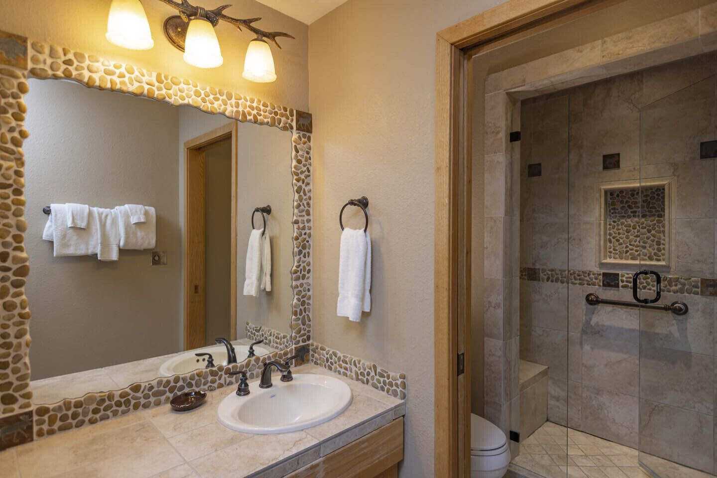 A bathroom with a stone mosaic backsplash, a large mirror, a sink with a faucet, and a shower area.